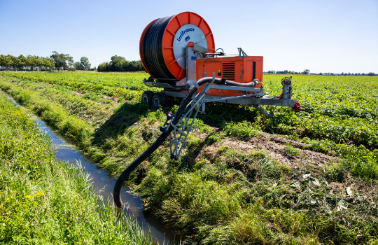 Een machine op landbouwgrond pompt water uit de sloot.