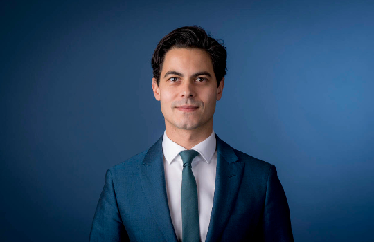 Portret van Rob Jetten tegen een blauwe achtergrond.