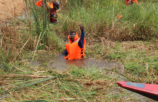 Een man in een oranje zwemvest staat tot zijn middel in het water en steekt zijn duim op.