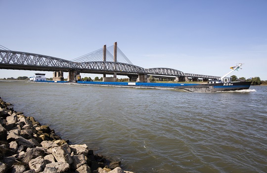 Een binnenvaartschip vaart onder een brug over de rivier de Waal door.
