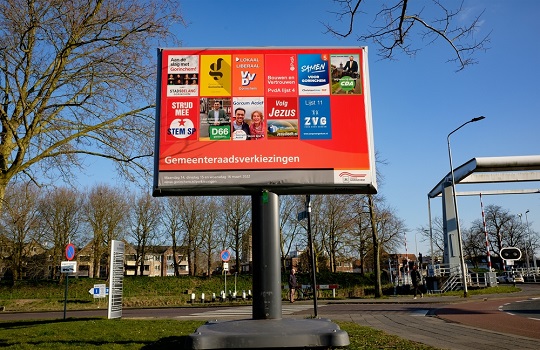 Een verkiezingsbord met posters van landelijke en lokale partijen.
