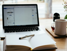 Laptop, notitieboekje en kop koffie op bureau