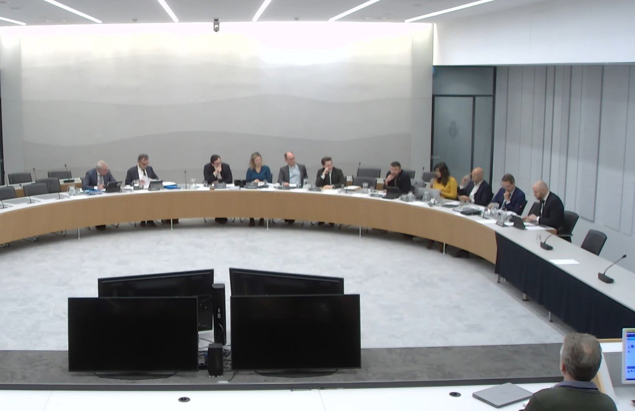 zaal met ronde tafel waaraan Tweede Kamerleden debatteren