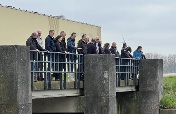 groep mensen op een brug bij waterschap De Dommel, erachter een loods en weiland