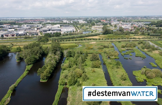 Luchtfoto van natuurgebied met waterpartijen en groene zones, grenzend aan de woonwijk Westergouwe. Rechtsonder staat de hashtag #destemvanwater waarmee de Unie van Waterschappen de belangen van de waterschappen onder de aandacht brengt rondom de Tweede Kamerverkiezingen van 2025.