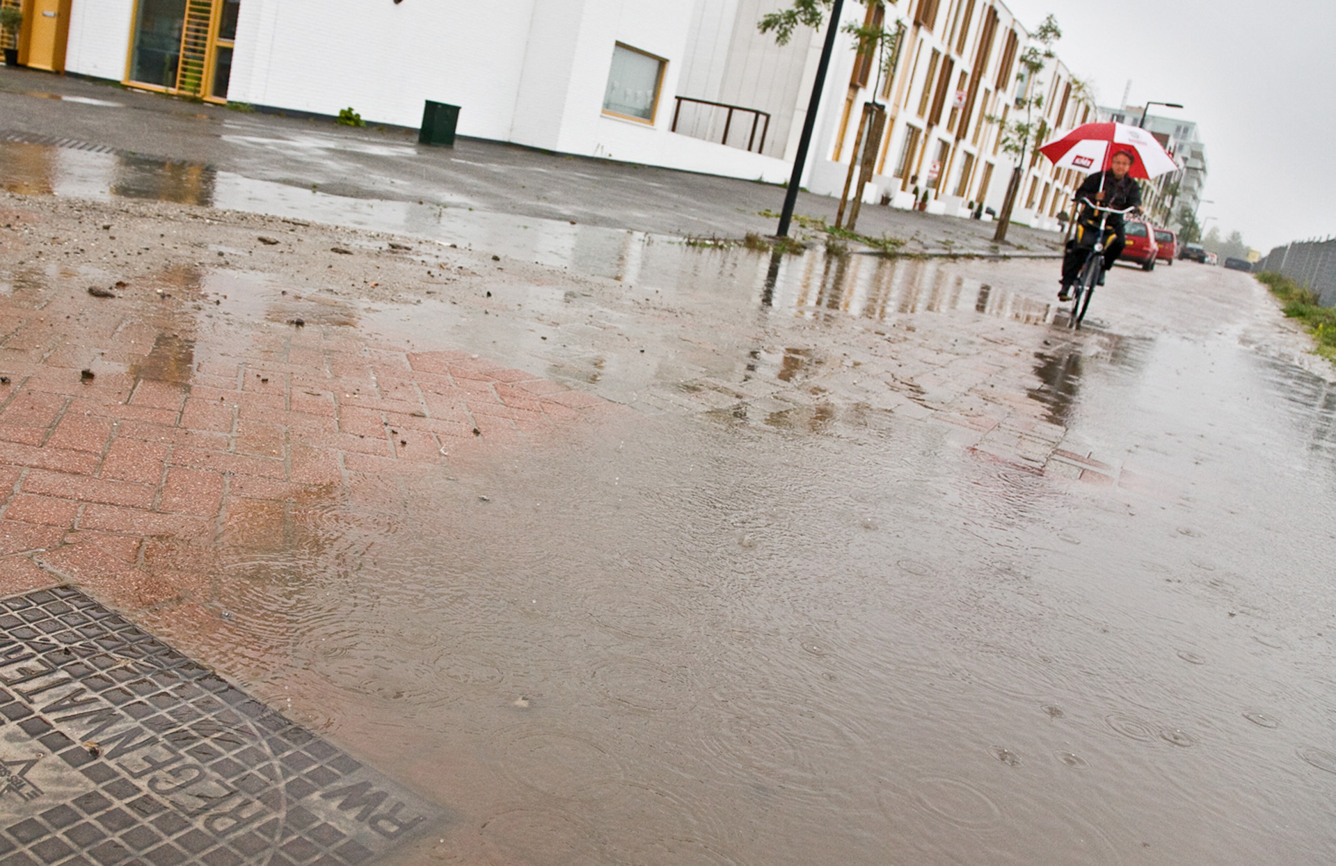 ondergelopen straat met in de verte een fietser met paraplu in de regen