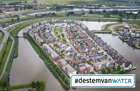 Luchtfoto van de woonwijk Westergouwe bij Gouda, omringd door water en groen, met de hashtag #destemvanWATER in beeld.