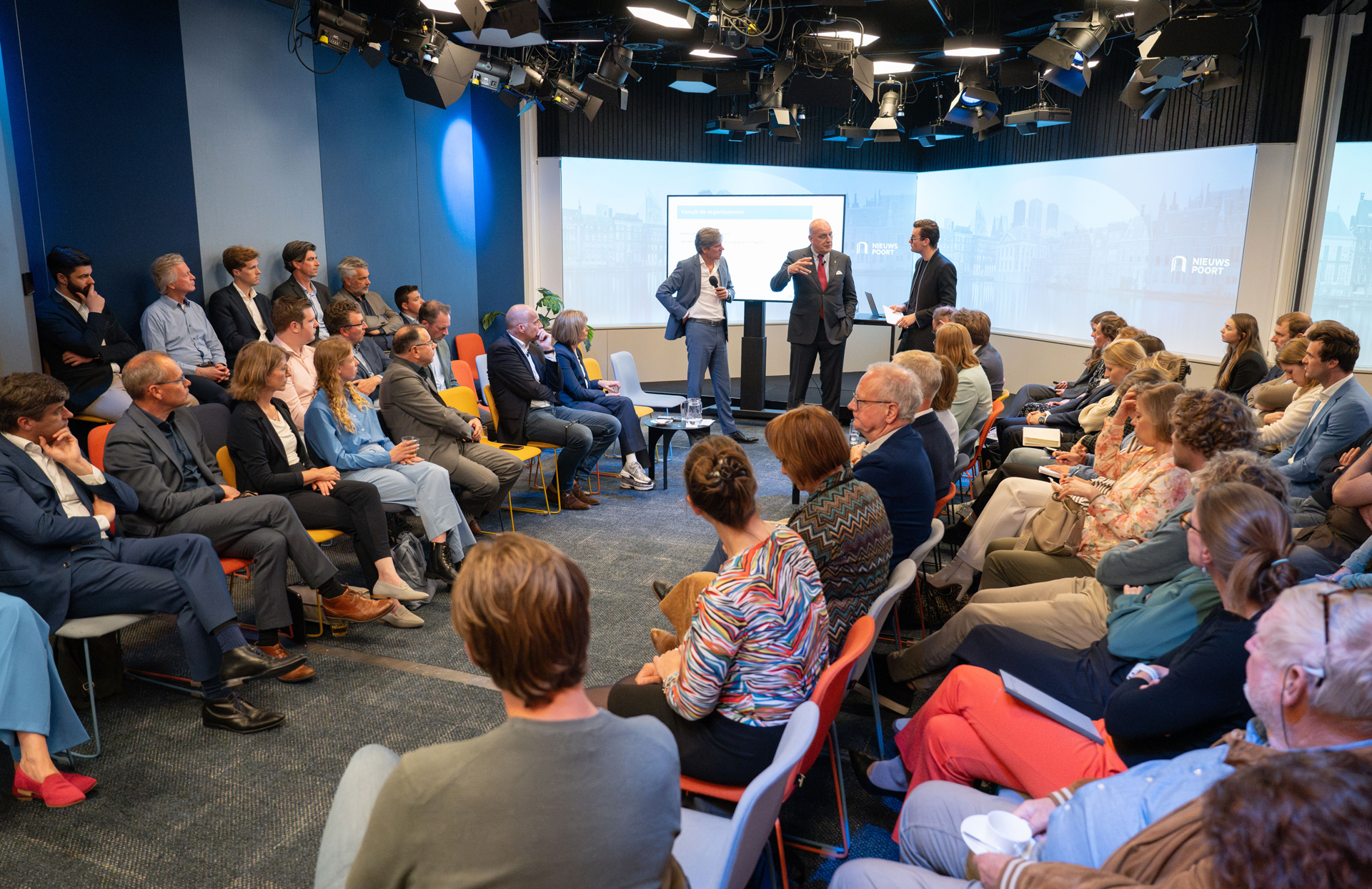 Een goedgevulde zaal luistert aandachtig naar Splinter Chabot, Vincent Lokin (bestuurslid Unie van Waterschappen) en Pieter Litjens (voorzitter Vewin). Ze staan voor een groot scherm in Nieuwspoort. De sfeer is zakelijk en betrokken. De deelnemers zitten in een halve cirkel, wat een interactieve setting suggereert.