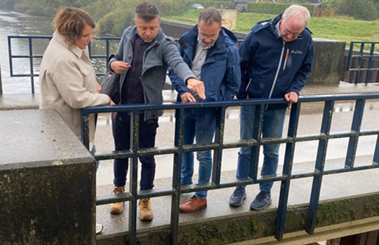 vier mensen op een brug boven rivier, kijken naar het water beneden